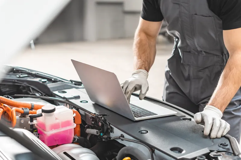 mechanic using laptop under vehicle hood